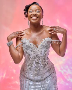 Zanele Potelwa Durban July 2025 in elegant silver dress with jewels, posing on a pink studio backdrop.