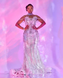 Zanele Potelwa Durban July 2025 in elegant silver dress with jewels, posing on a pink studio backdrop.