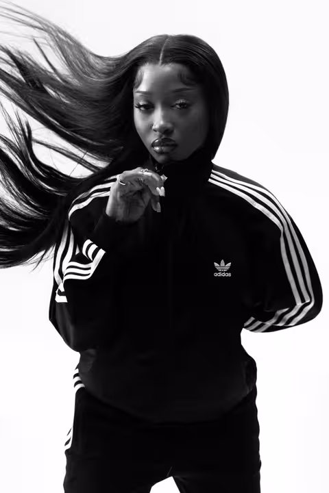 A black and white portrait of Uncle Waffles wearing a black adidas tracksuit, with her long hair flowing dramatically.