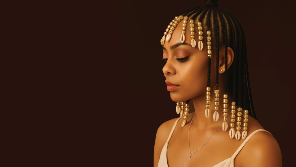 A beautiful woman with intricate braided hair adorned with cowrie shells and golden beads, celebrating the HAIR-itage Mall of Africa campaign.