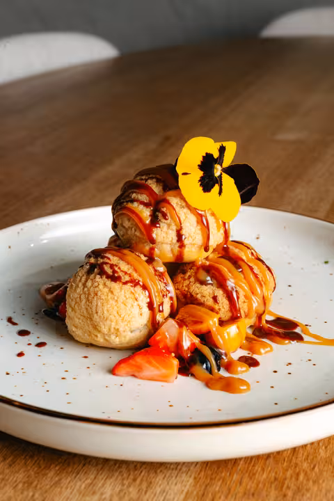 Exquisitely plated dessert from the Temptation Thursday three-course menu at Tempo Luxury Restaurant, featuring profiteroles drizzled with caramel sauce and a yellow edible flower.