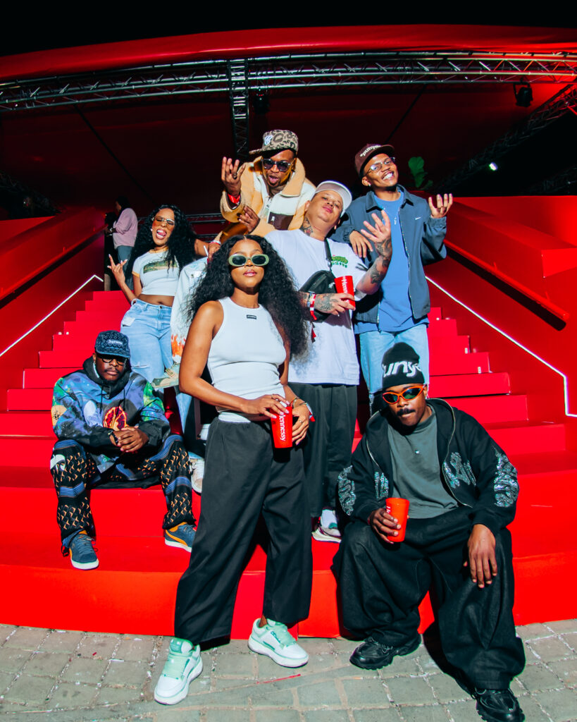 A group of stylish South African hip-hop and fashion figures posing together on a grand red staircase at a event.