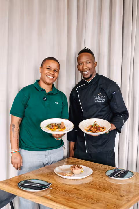 Chef Bonga Williams and Nompumelelo posing together, holding two plated dishes from the Tempo Luxury Restaurant menu.