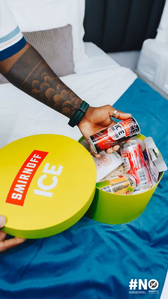 A hand holding a Smirnoff ICE can over a yellow and lime green welcome box containing snacks and gifts for the Fon City event.